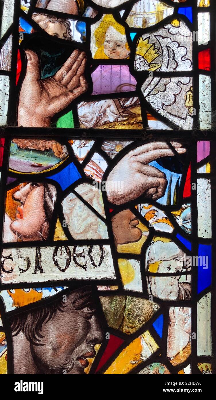 Una hermosa ventana compuesta de coloridas vidrieras medievales con muy diversos rostros expresivos, manos y algunos scrip medieval. Foto de stock