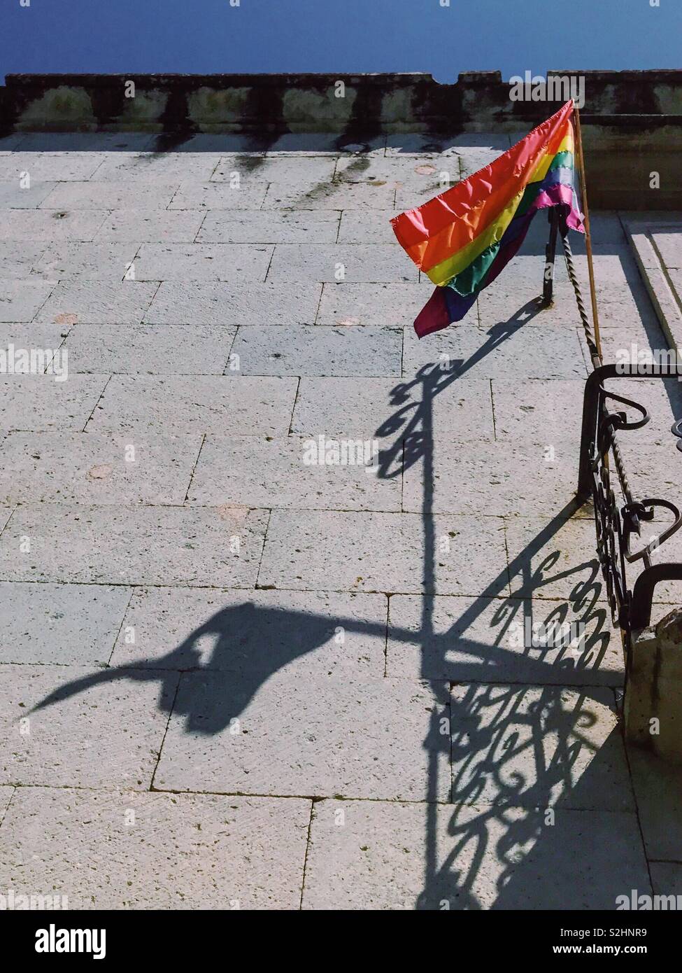 B-side de lado brillante. Brillante bandera LGBTQ desgarrado y su sombra sobre la pared de la casa. A menudo detrás de un aspecto brillante no vemos el sufrimiento escondido y traumas. Oaxaca, México. 16 de febrero de 2019 Foto de stock