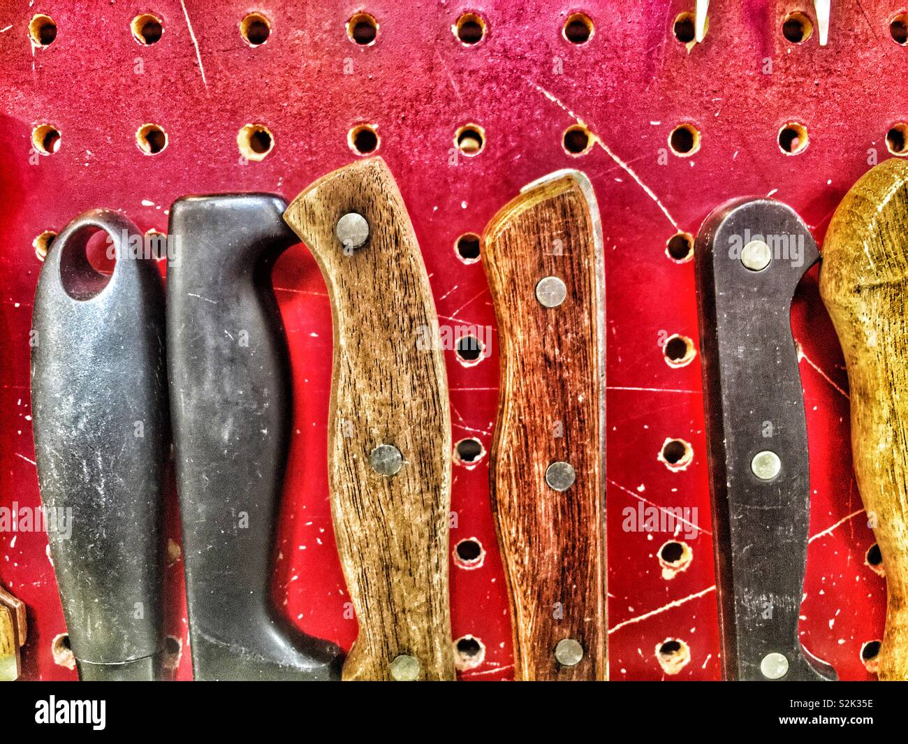 Mangos de cuchillos de madera antigua correctamente almacenados contra una  pared roja junta de peg Fotografía de stock - Alamy