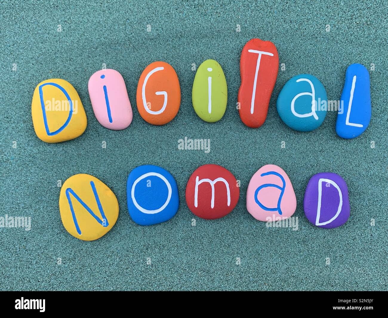 Nómada Digital, nuevo perfil de trabajo texto compuesto con piedras marinas multicolores en arena verde Foto de stock
