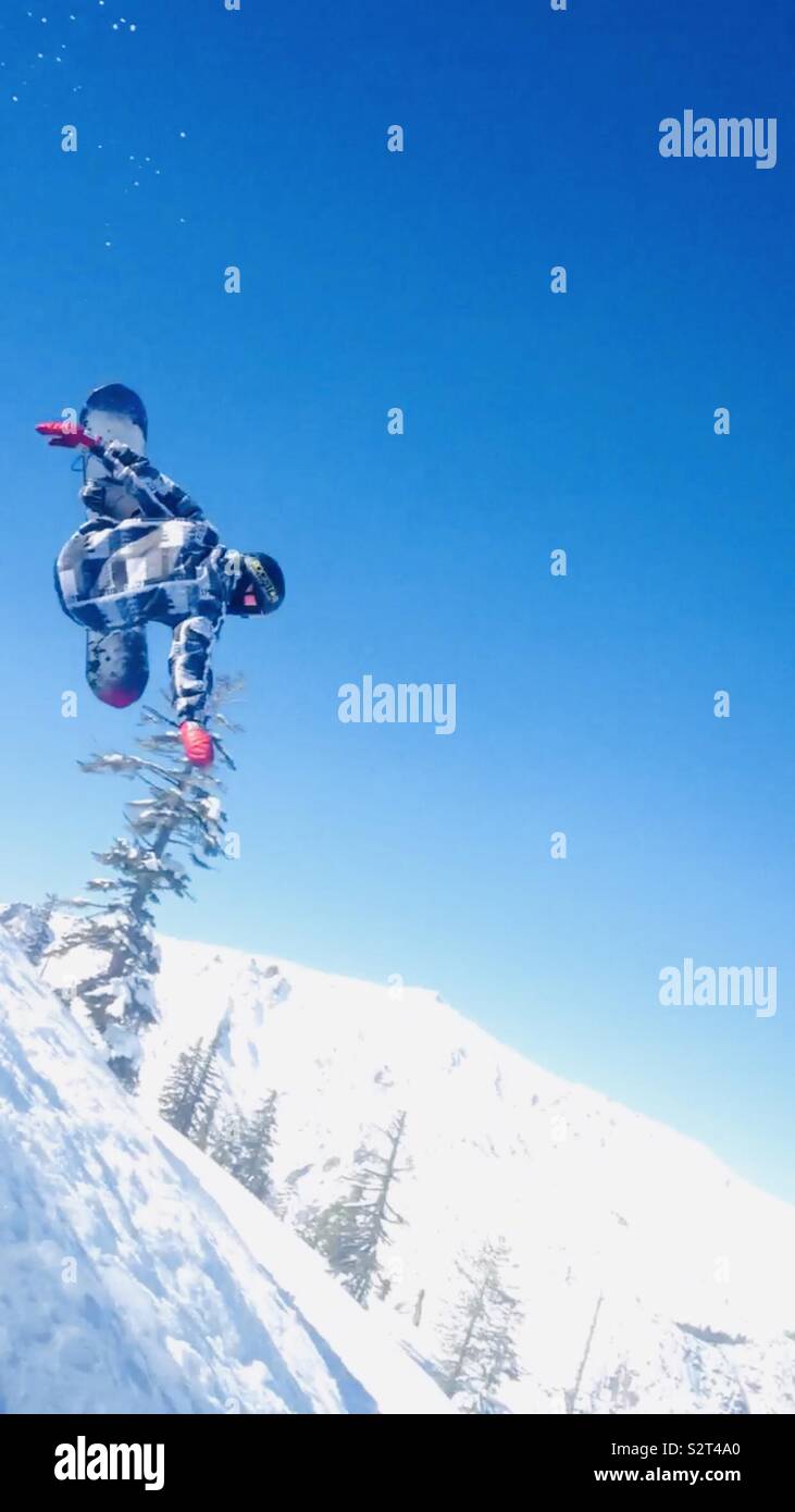 Bear Valley Ski Resort, en el norte de California. Snowboarder haciendo un truco en el aire en un día hermoso con un cielo azul. Guantes vestidos de rojo, blanco y negro chaqueta. Foto de stock