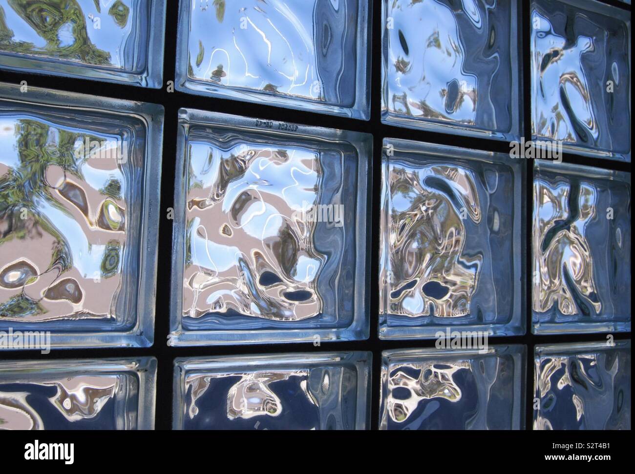 Pared de vidrio con mini plazas reflejando el azul y el verde y el sol brilla a través de mostrar el reflejo de los árboles y el cielo Foto de stock