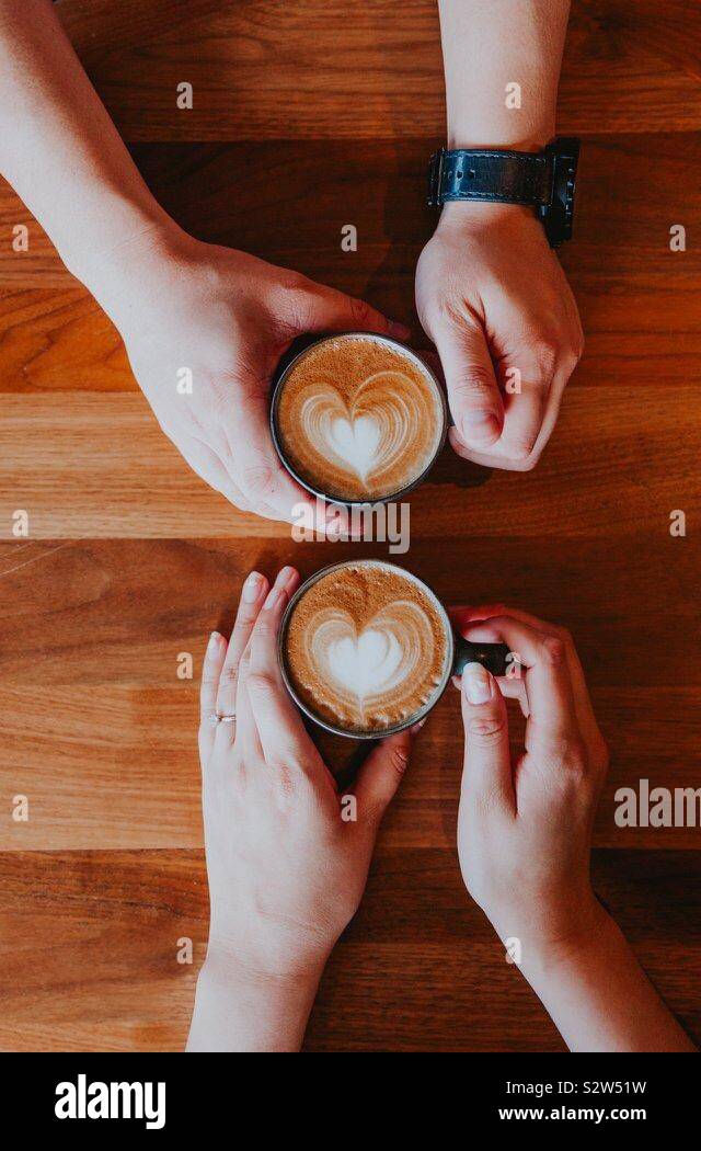 Dos tazas de café latte art en una tabla. Dos personas sosteniendo tazas de café. Foto de stock