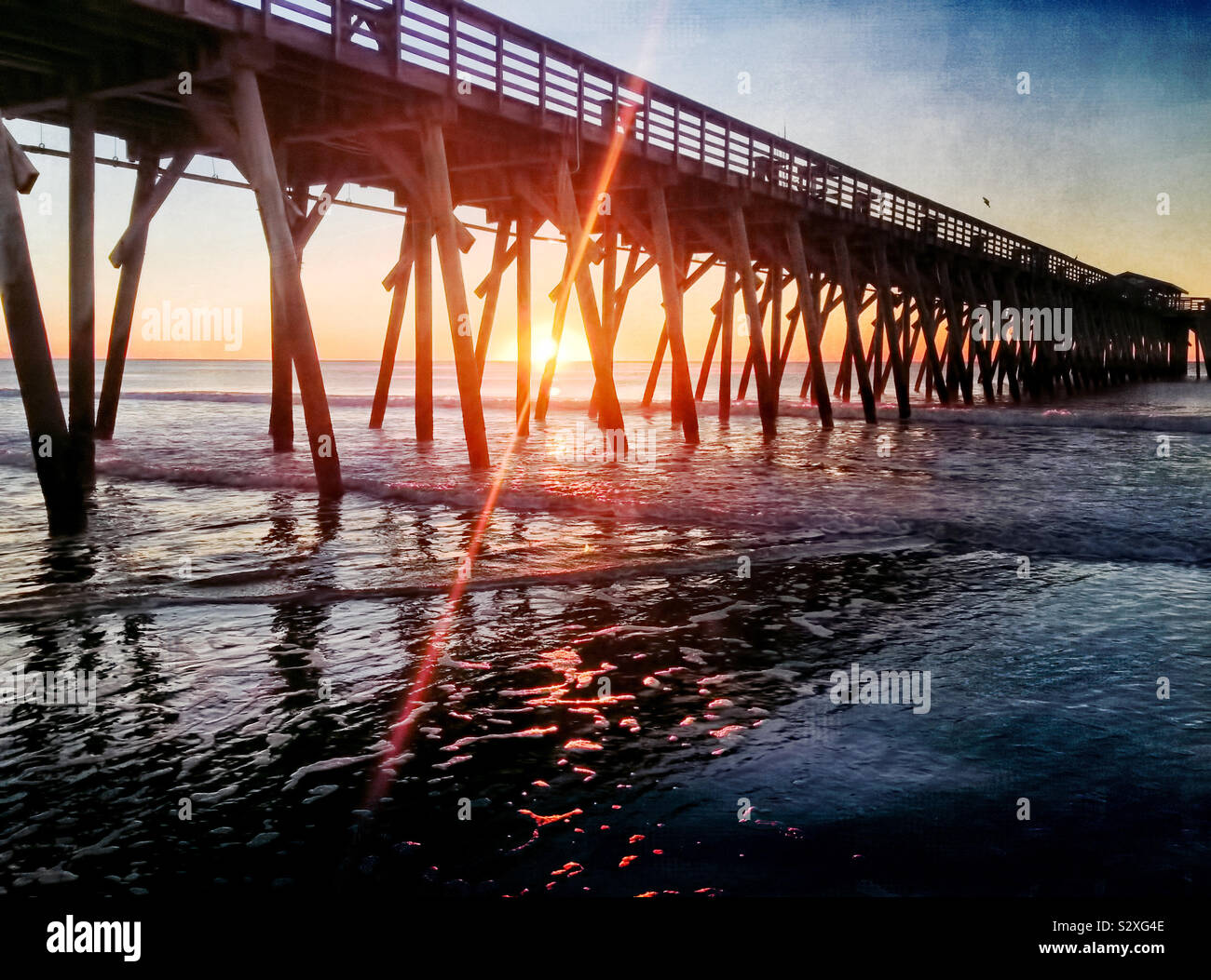 Amanecer detrás de un muelle en Myrtle Beach, Carolina del Sur. El brillante destello de lente desde el sol naciente crea interés visual. Foto de stock