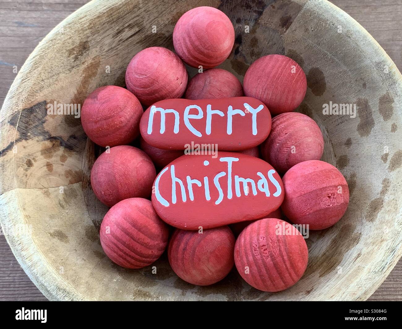 Feliz Navidad mensaje tallados y pintados en dos piedras en una cesta con bolas de madera roja Foto de stock