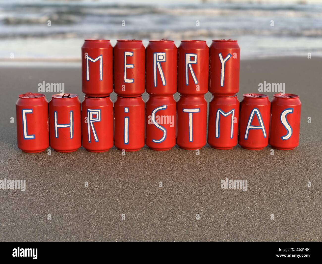 Feliz Navidad mensaje pintado en rojo el estaño latas de cerveza en la playa Foto de stock