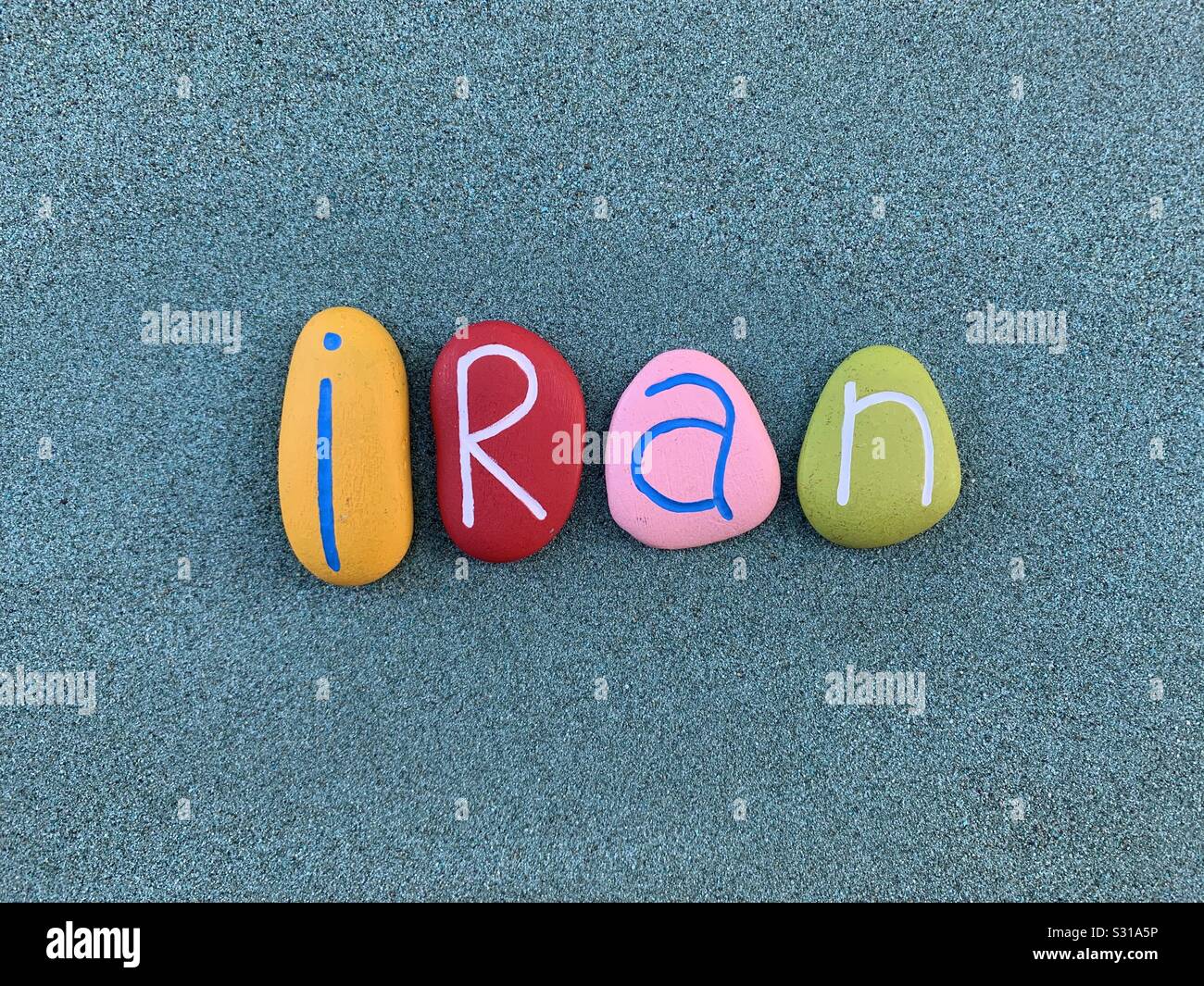 Irán, República Islámica de Irán, país en el Asia occidental, recuerdo con piedras multicolores letras en arena verde Foto de stock