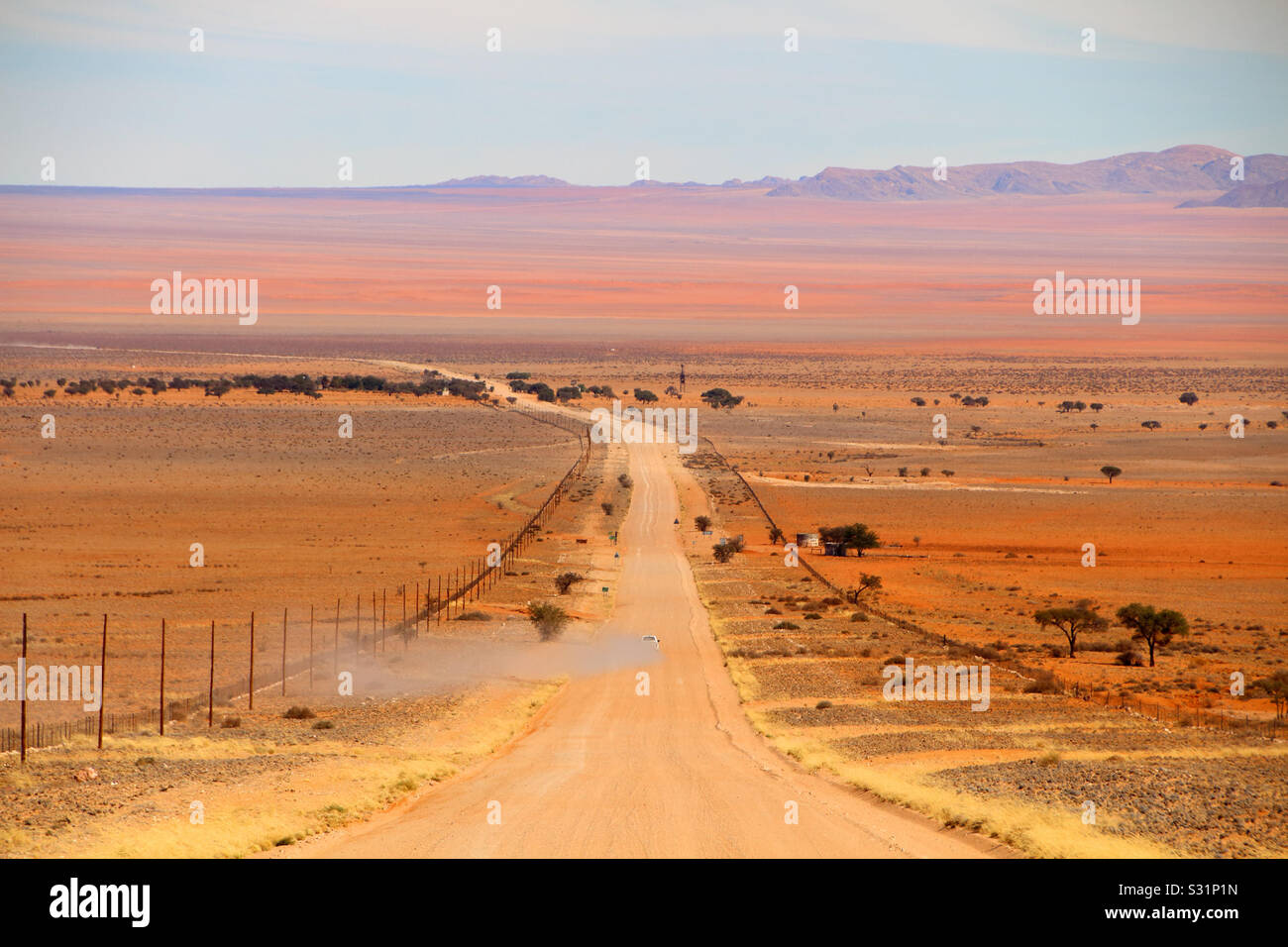 Perspectiva mirando un hermoso paisaje como un automóvil lanza una nube de polvo en un camino de tierra. Foto de stock