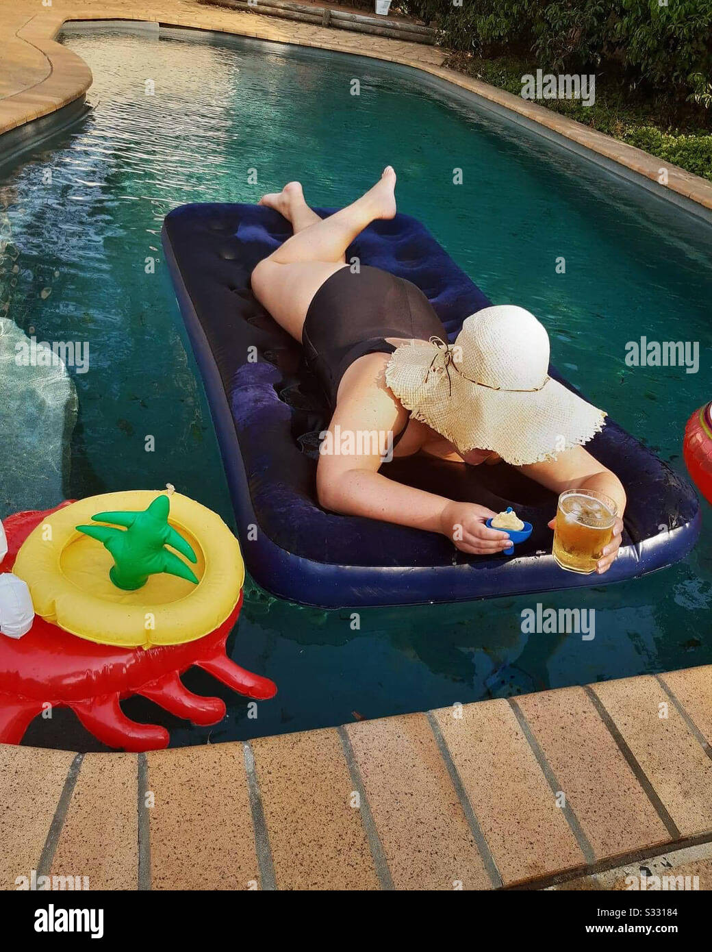 Persona tumbada en un flotador en una piscina. Celebración de una cerveza y  un refresco de hielo. Un sombrero está protegiendo su cara Fotografía de  stock - Alamy