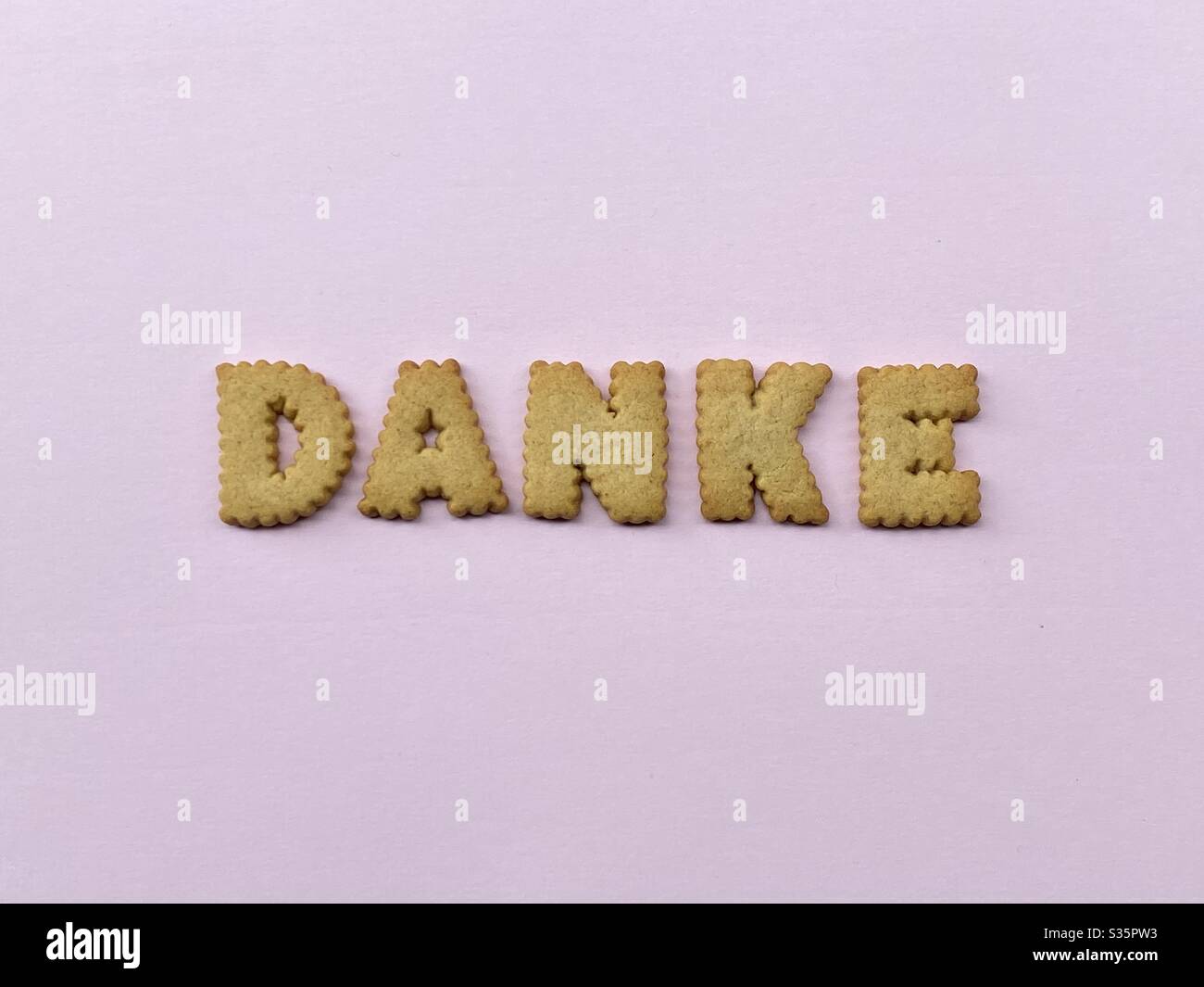 Danke, palabra alemana que significa gracias compuesto con letras caseras galletas sobre color rosa Foto de stock