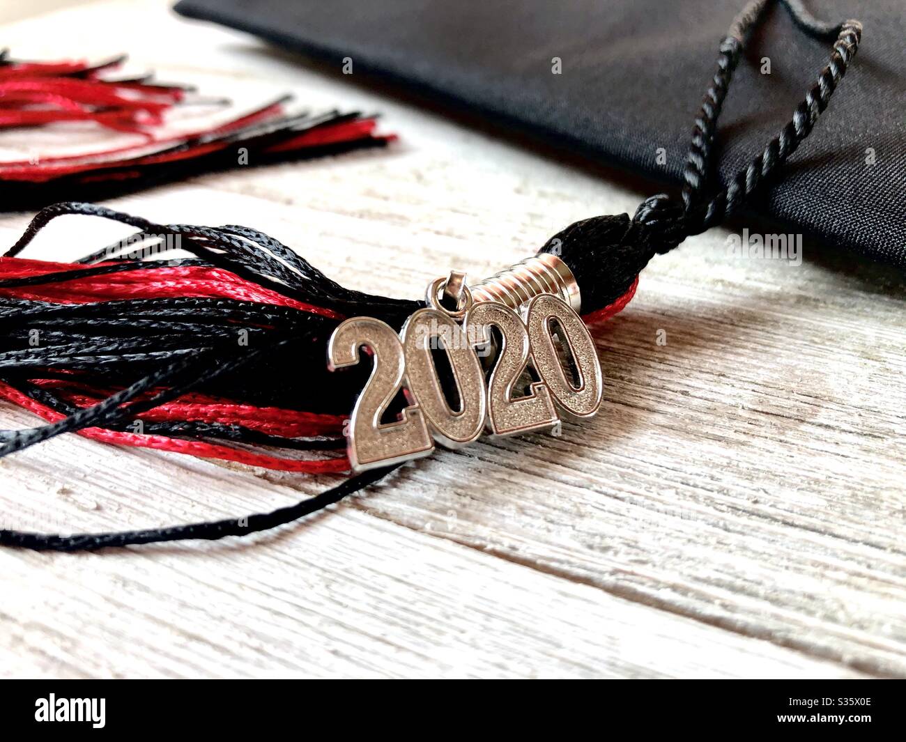Gorra de graduación roja y negra 2020 y borla sobre una superficie de madera Foto de stock