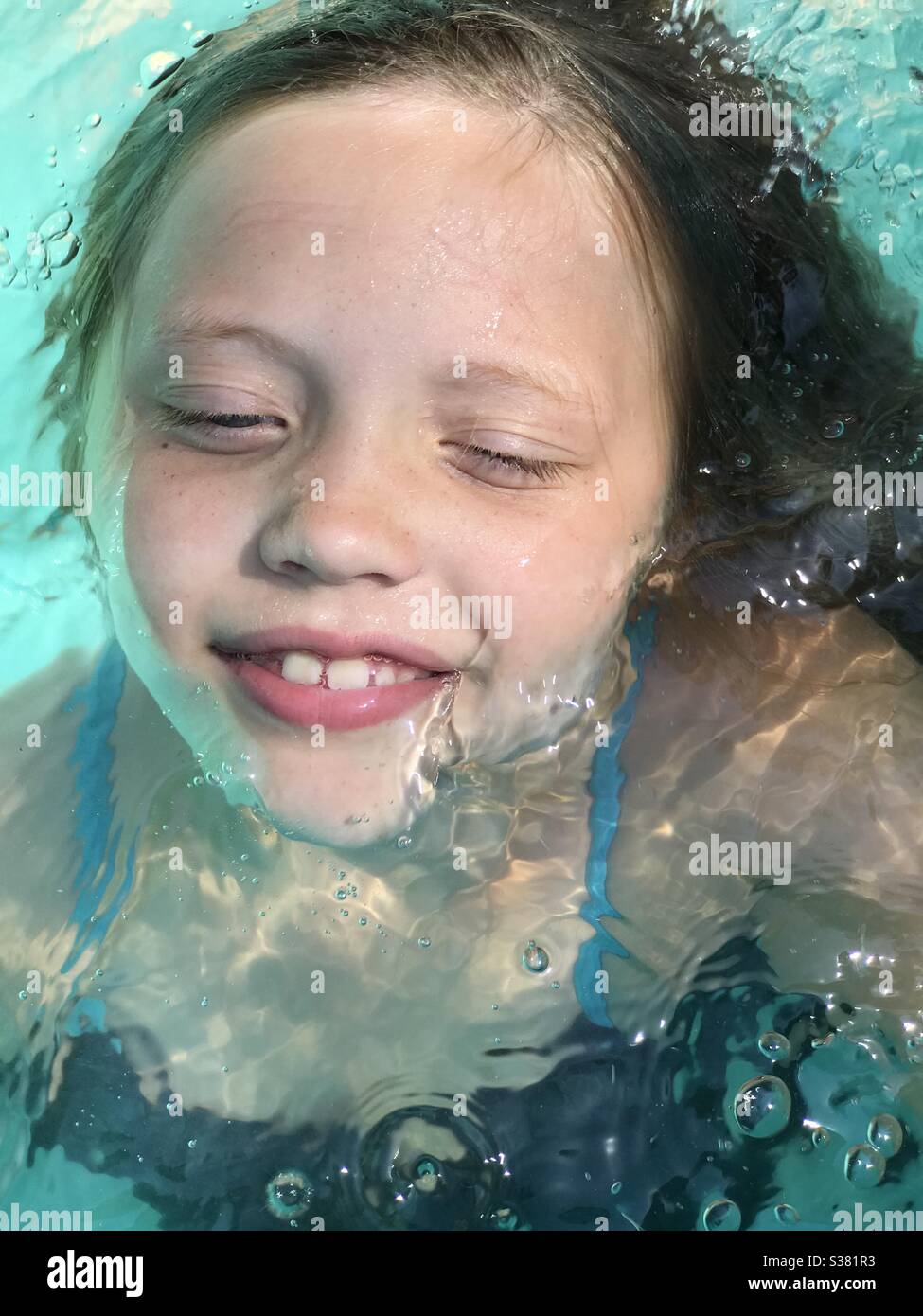 La cara de la niña se pegaba del agua, sonriendo en la piscina. Parece relajado Foto de stock