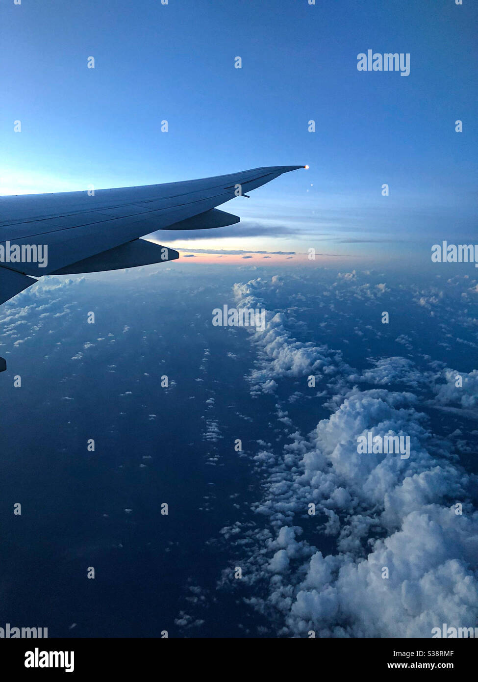 Una vista del cielo al amanecer desde una ventana de avión que muestra algunas nubes y el ala del avión. Foto de stock