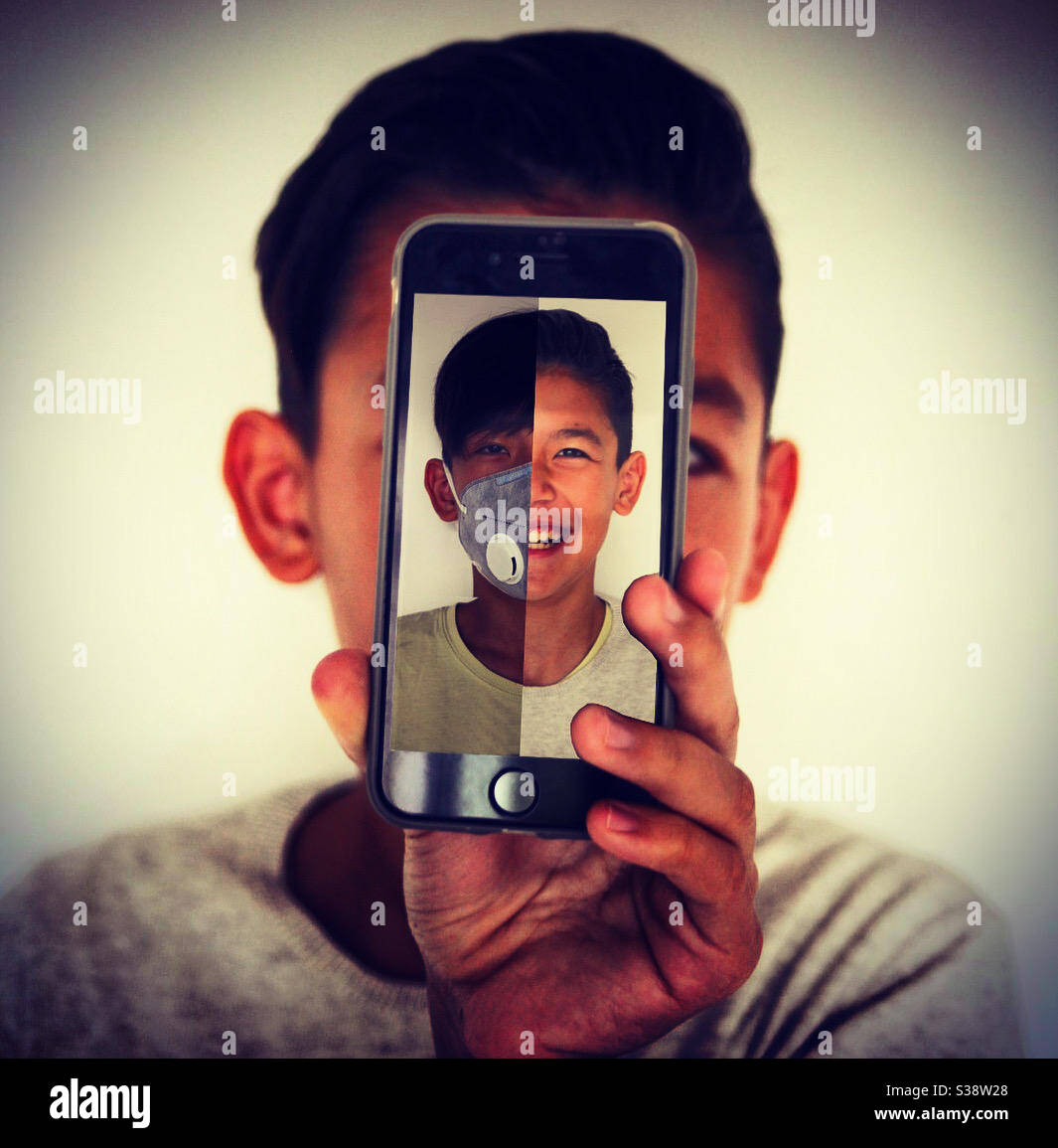 Durante el covid-19, un joven asiático creativo lleva una mitad de cara en la pantalla de su smartphone Foto de stock