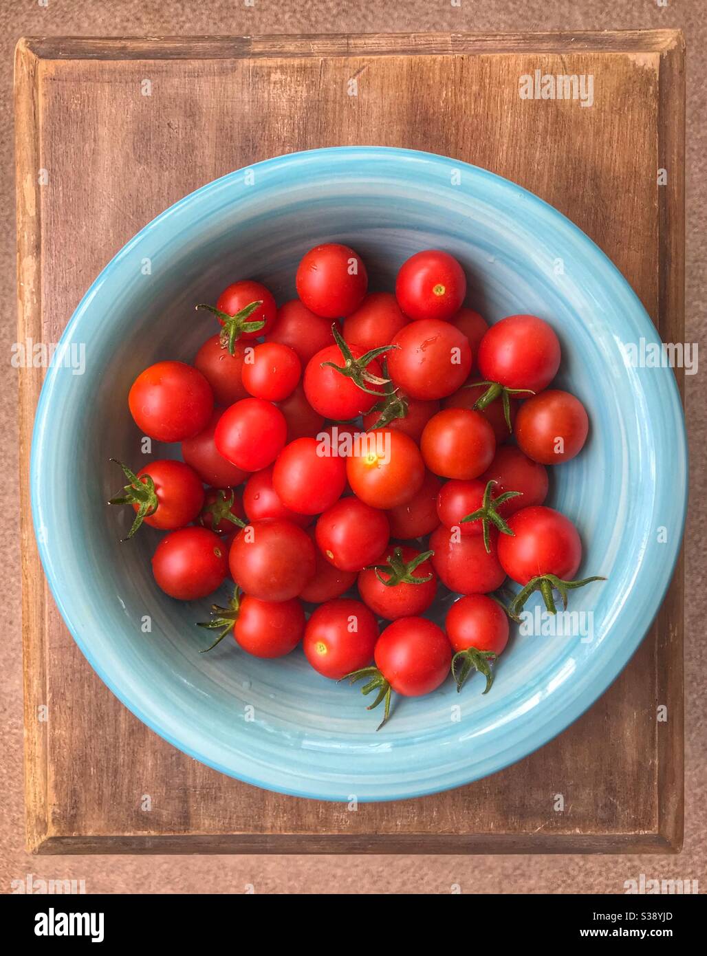 Tomates cherry en cuenco azul sobre una pequeña mesa de madera Foto de stock