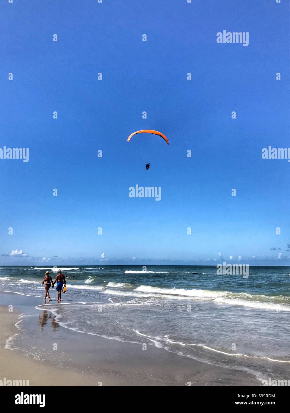 Un par camina por la playa mientras un parapente vuela por Jacksonville Beach, Florida Foto de stock