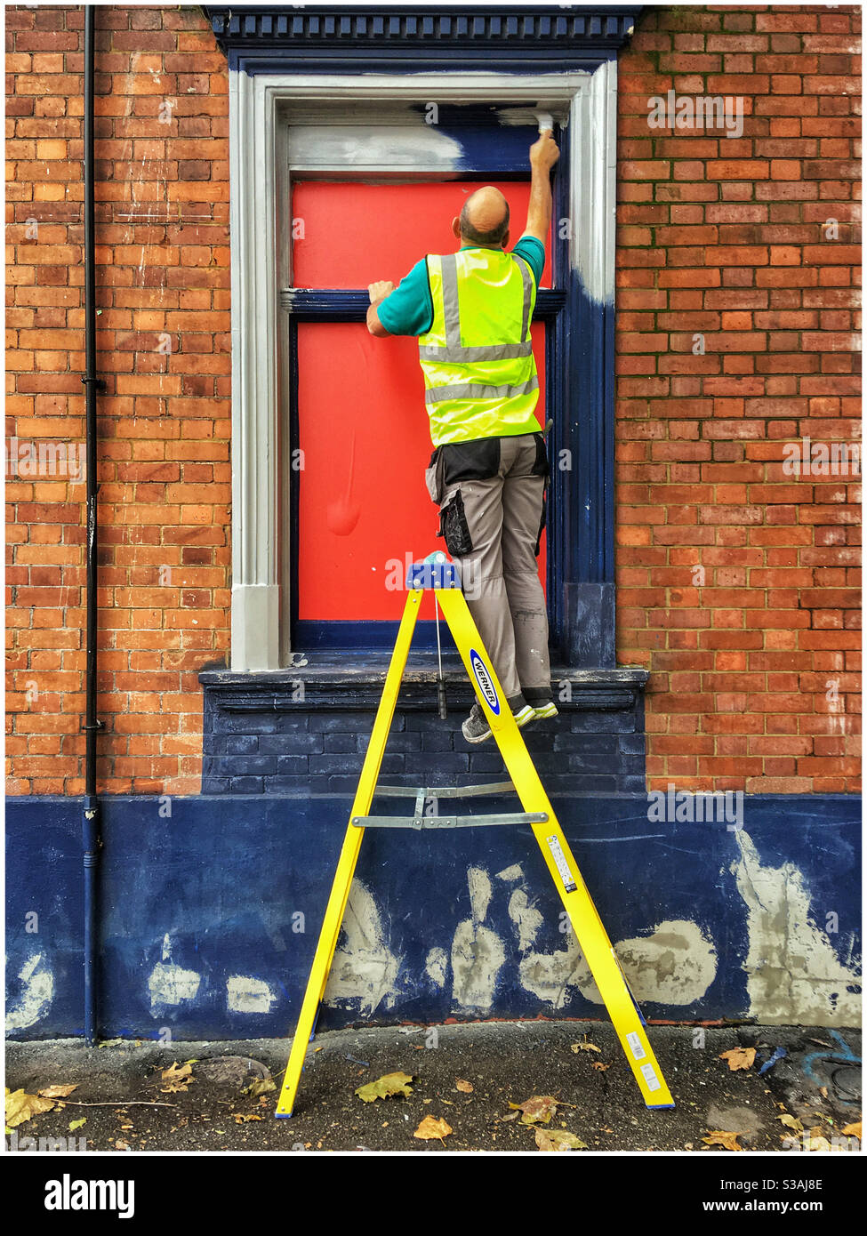 Hombre de alta visibilidad vest arriba una escalera que pinta una ventana marco Foto de stock
