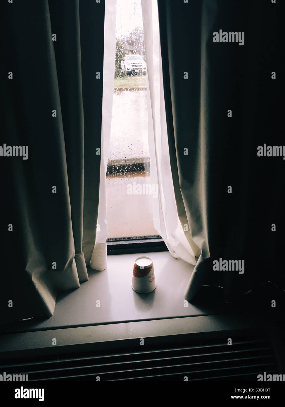 Vieja taza de café en la ventana del motel en la mañana lluviosa Foto de stock