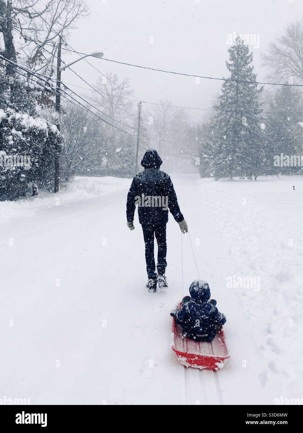 Un papá tirando de su hijo en un trineo por una calle nevada en el suburbano de Nueva Jersey, Estados Unidos. Foto de stock