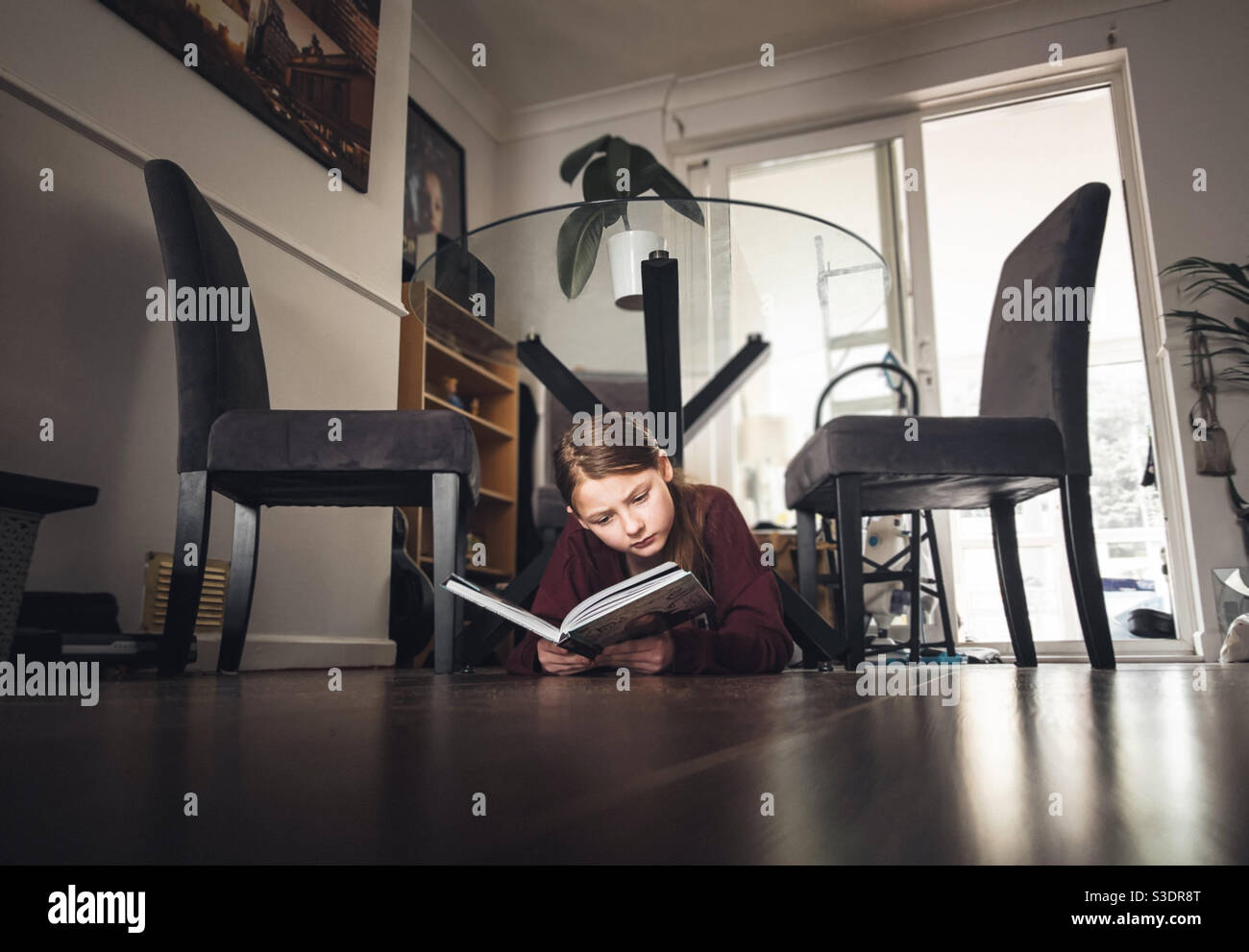 Chica lee un libro bajo una mesa Foto de stock