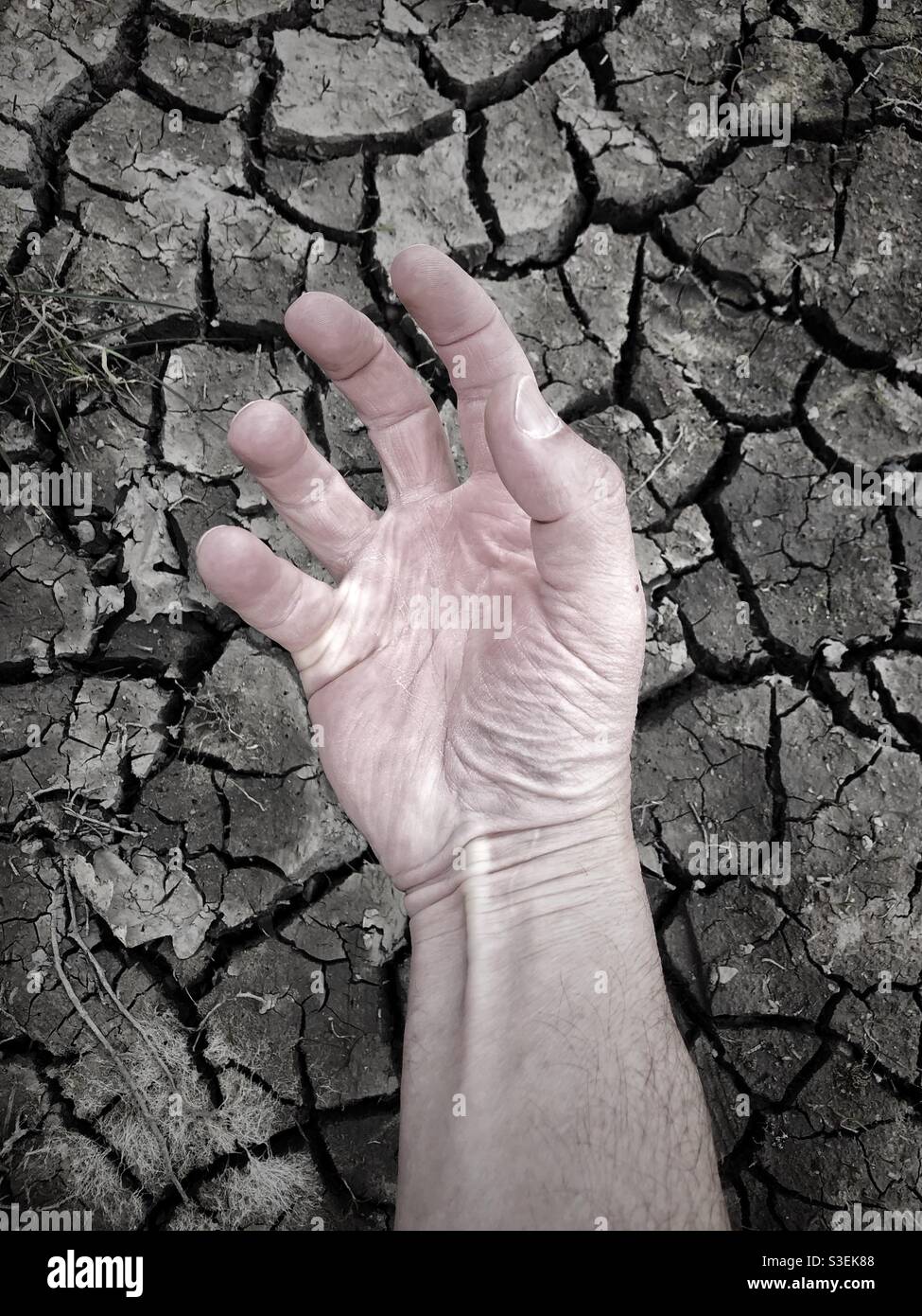 Concepto de sequía y calor con lecho de río seco y agrietado y la piel seca en una mano humana que alcanza para el agua Foto de stock