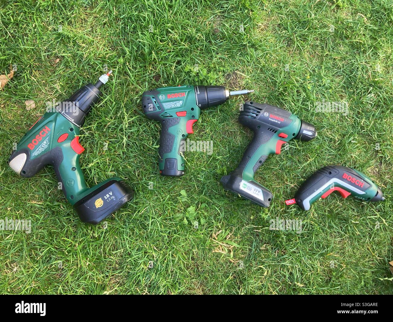 Cuatro taladros eléctricos Bosch y destornilladores de diferentes tamaños en la hierba Foto de stock
