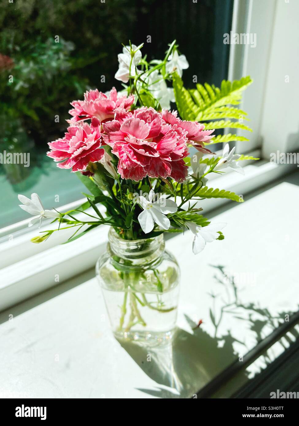 Una jarra de cristal pequeña con un arreglo floral bonito en un alféizar de la ventana. Foto de stock