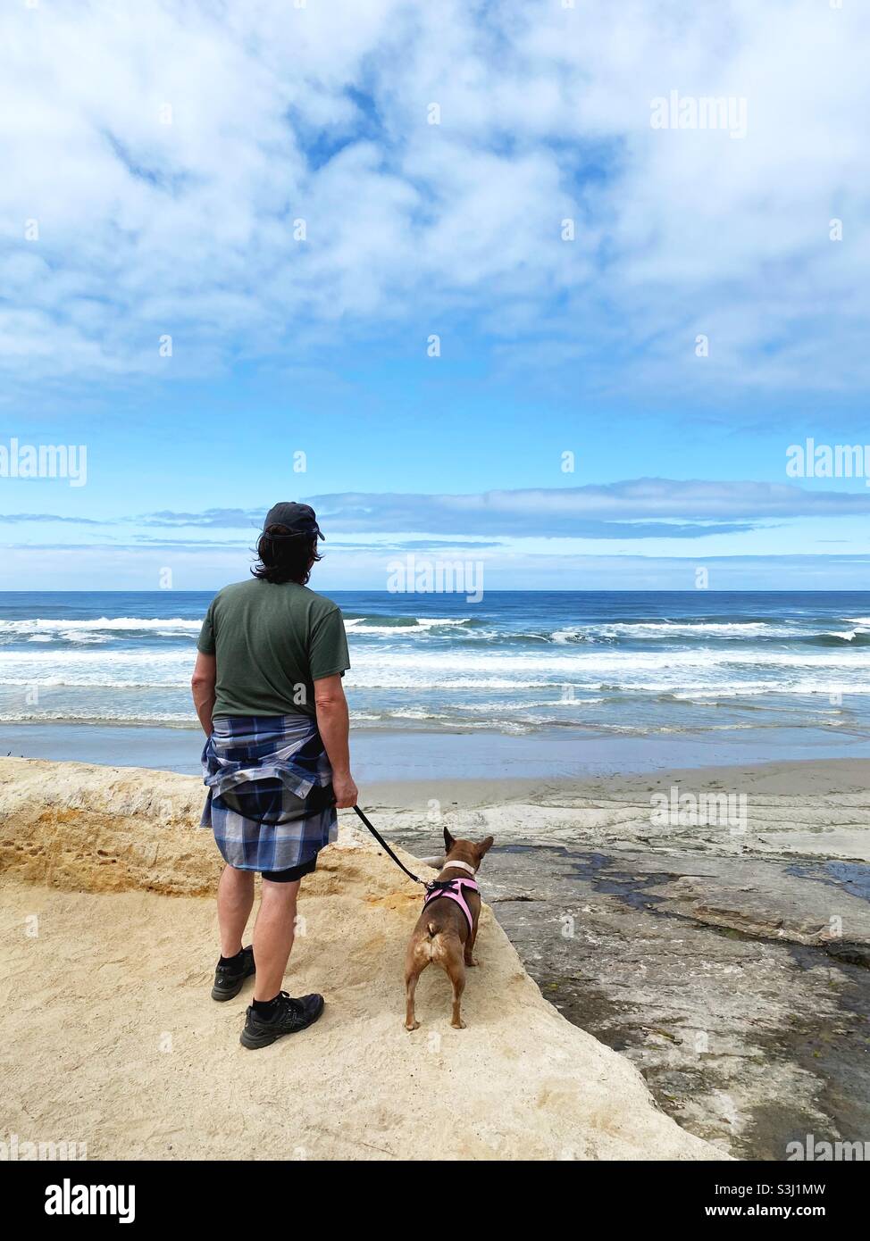 Un hombre de pie con un bulldog francés mirando al océano en Yachats, Oregon. Foto de stock