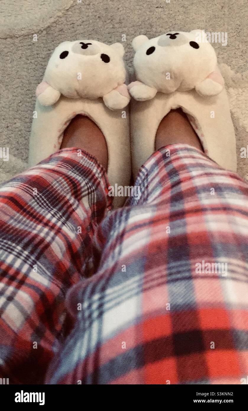 Piernas con pijamas rojos y pantuflas blancas de oso Foto de stock