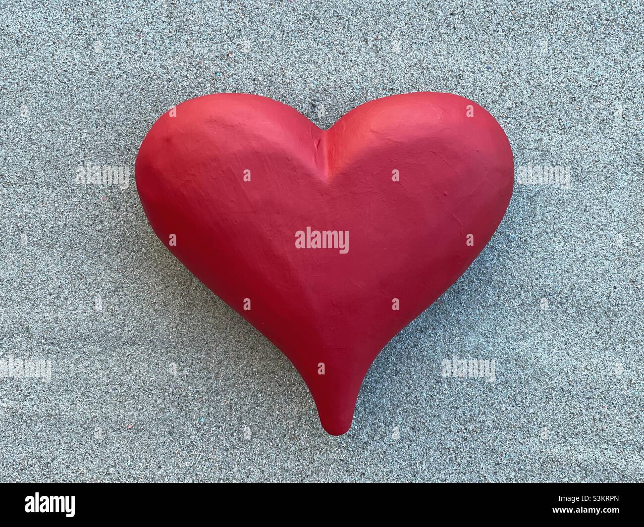 Corazón de piedra pintado a mano rojo grande sobre arena verde Foto de stock