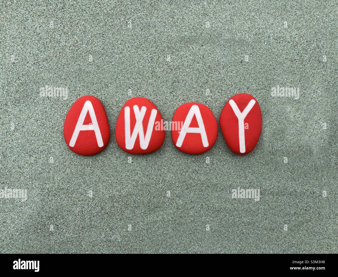 Lejos, mensaje creativo compuesto con letras de piedra roja pintadas a mano sobre arena verde Foto de stock