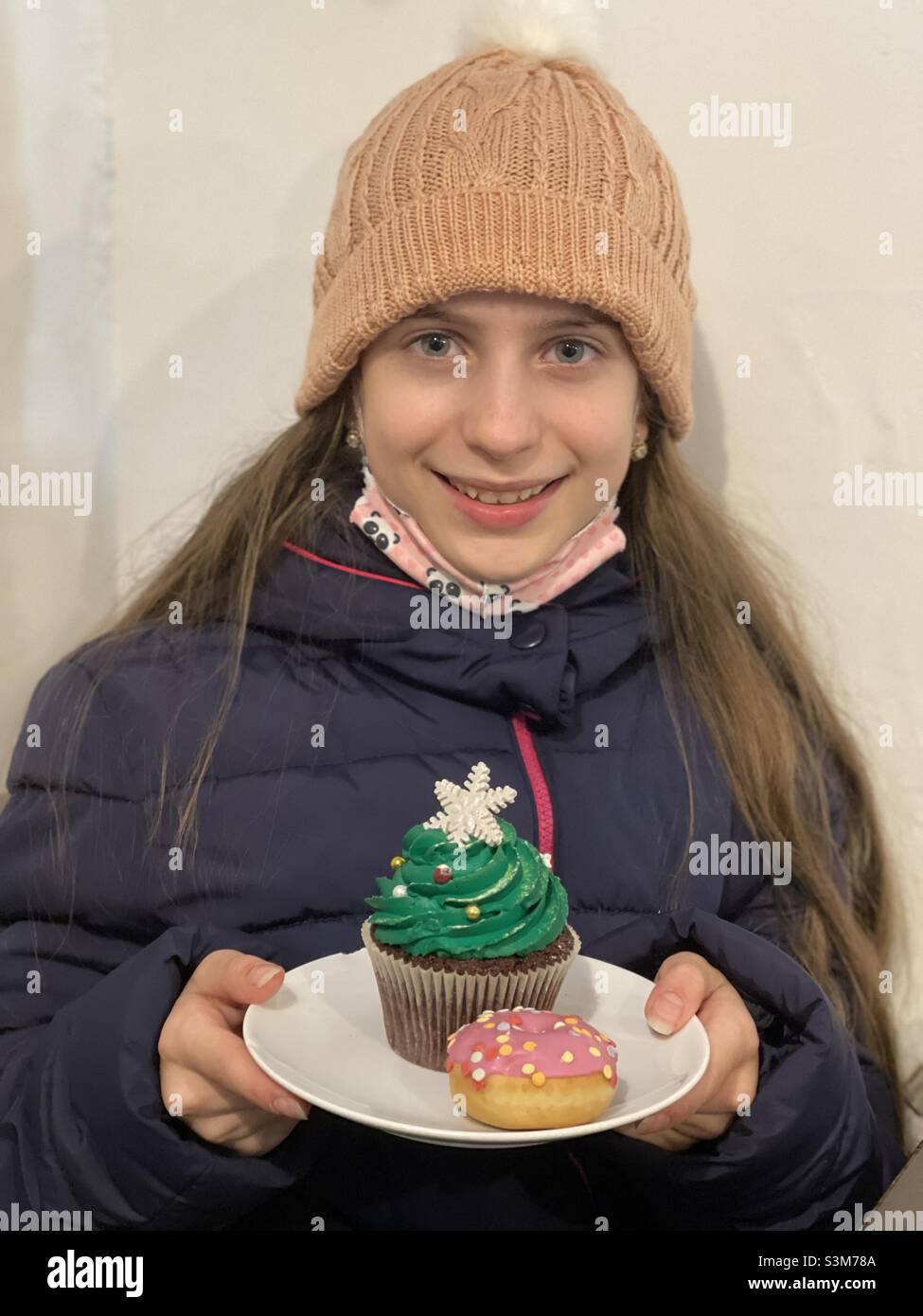 Feliz niña con un pastel de Navidad y un colorido donut en el bar Foto de stock