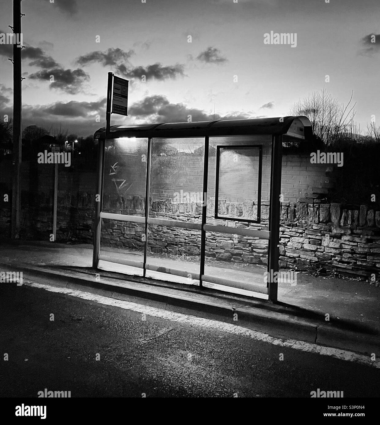 'La parada de autobús' Una parada de autobús rural está bien iluminada, no en consonancia con sus alrededores, con graffiti y vandalismo expuestos en una pared de piedra seca como telón de fondo (blanco y negro) Foto de stock