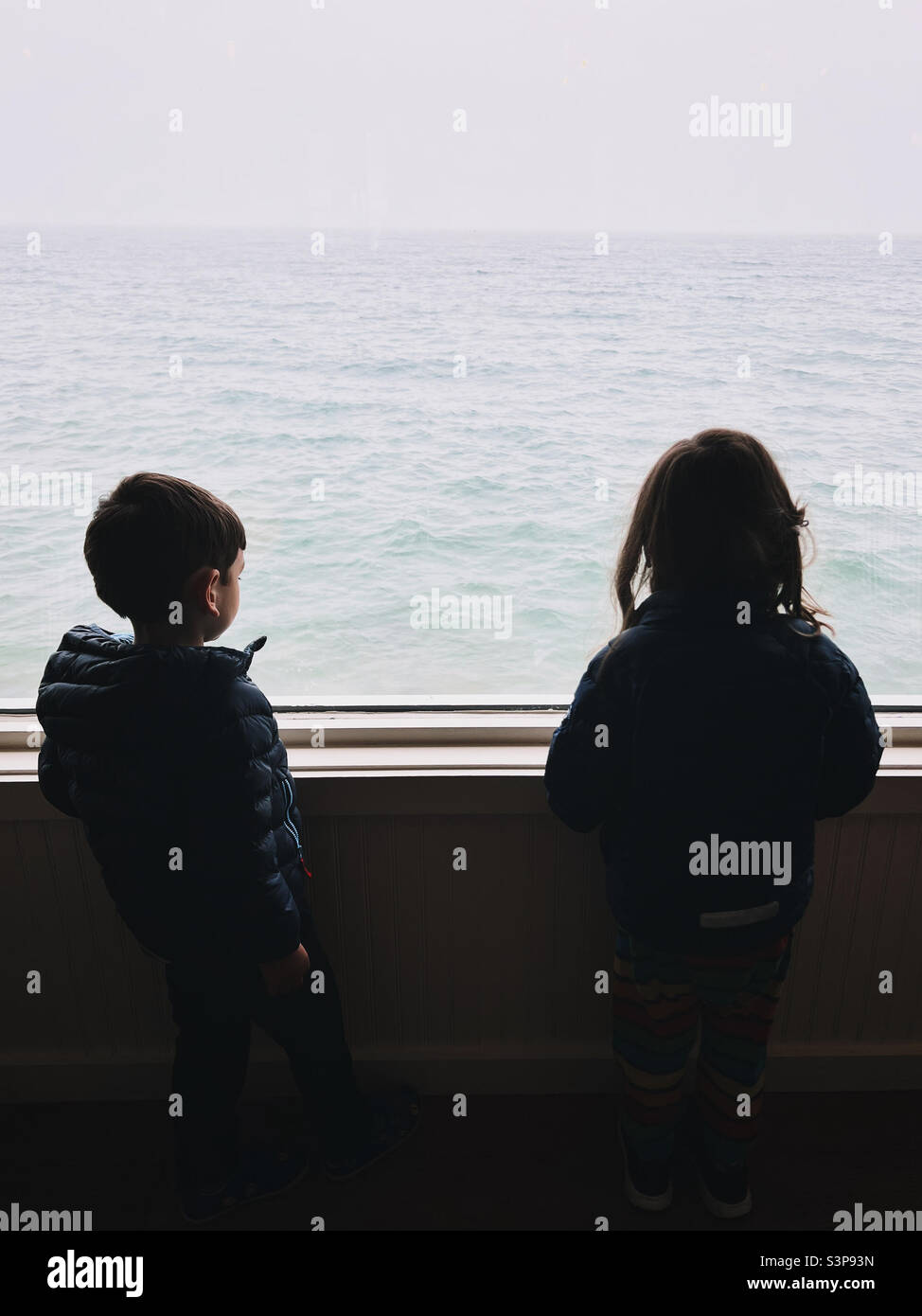 Un niño y una niña mirando por una ventana en el Long Island Sound, NY, Estados Unidos. Foto de stock