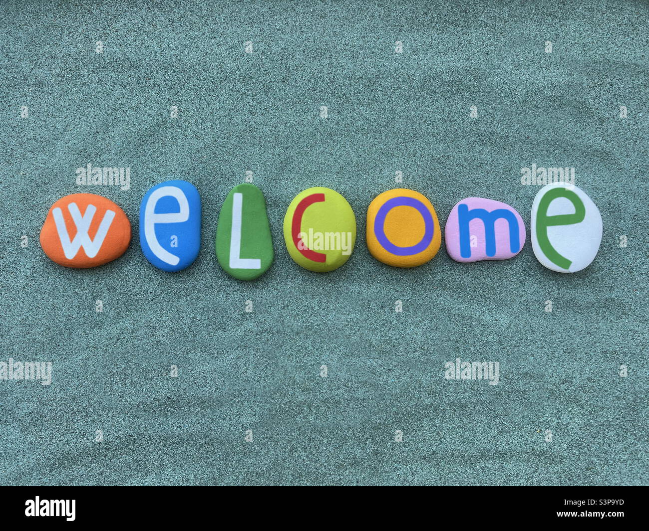 Texto de bienvenida compuesto por letras de piedra multicolor sobre arena verde Foto de stock