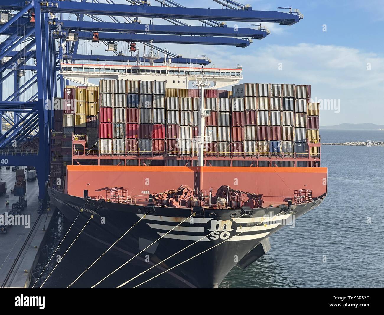 Un enorme buque contenedor completamente cargado de la compañía MSC bajo la operación de carga está amarrado con cuerdas al muelle en la terminal de carga en el puerto de Piraeus, Grecia. Vista para el arco con el logotipo de la empresa. Foto de stock