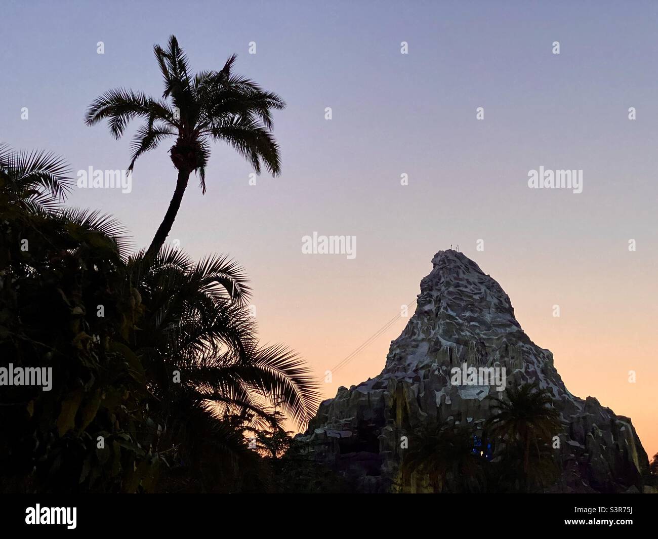 ANAHEIM, CA, 2021 DE JULIO: Cima de la montaña Matterhorn, atracción en Disneyland, con la silueta de palmeras y el cielo del atardecer Foto de stock