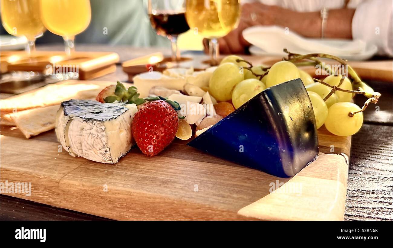 Plato de queso y fruta con cervezas artesanales en una tabla de servir de madera Foto de stock