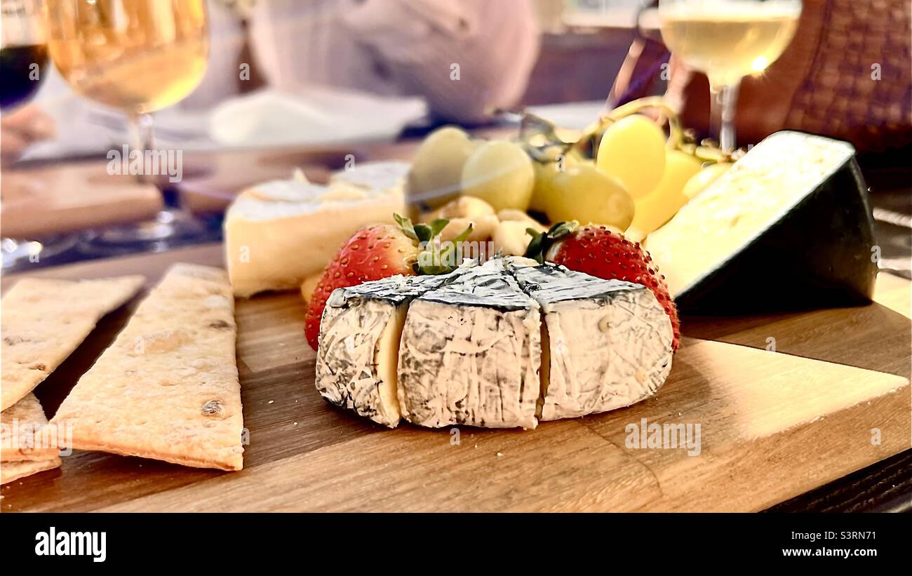 Plato de queso y fruta en una tabla de servir de madera con vuelos de cerveza Foto de stock