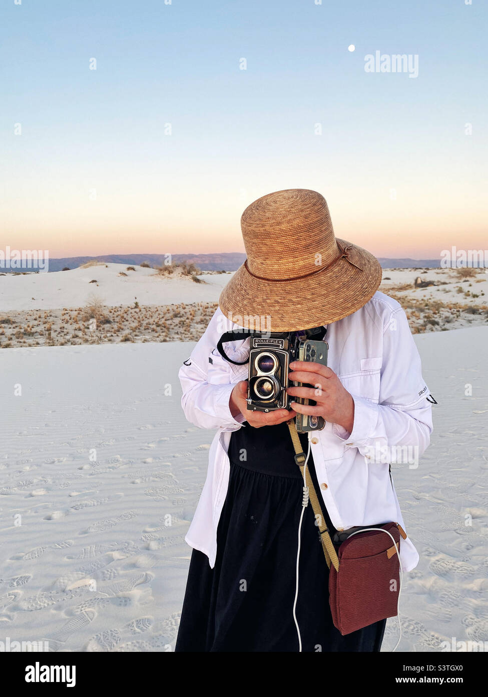 Fotógrafo con cámara analógica fotografiando durante la puesta de sol en el monumento nacional de arenas blancas de Nuevo méxico Foto de stock
