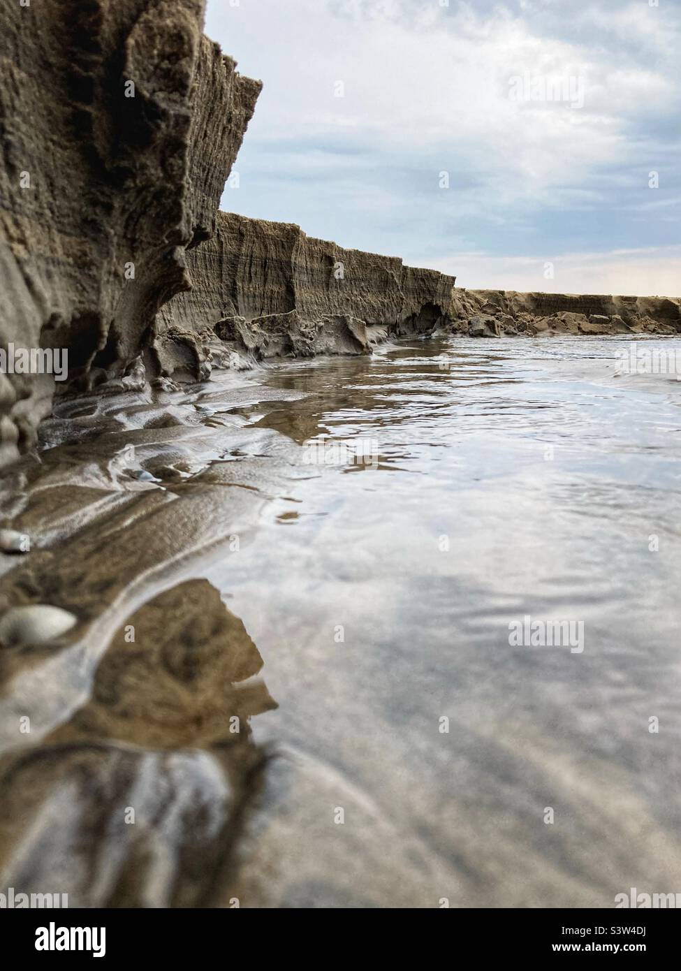 Primer plano de la escarpa de un pequeño río que cruza una playa y desemboca en el mar Báltico dando la impresión de ser un gran acantilado, de sólo unos 20 cm de altura en realidad Foto de stock