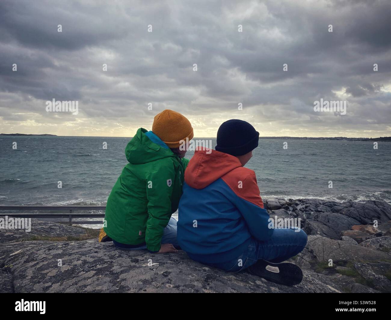 Dos hermanos o amigos a las edades de ocho o nueve años y once o doce observando el mar báltico en la costa oeste sueca durante una tormenta Foto de stock
