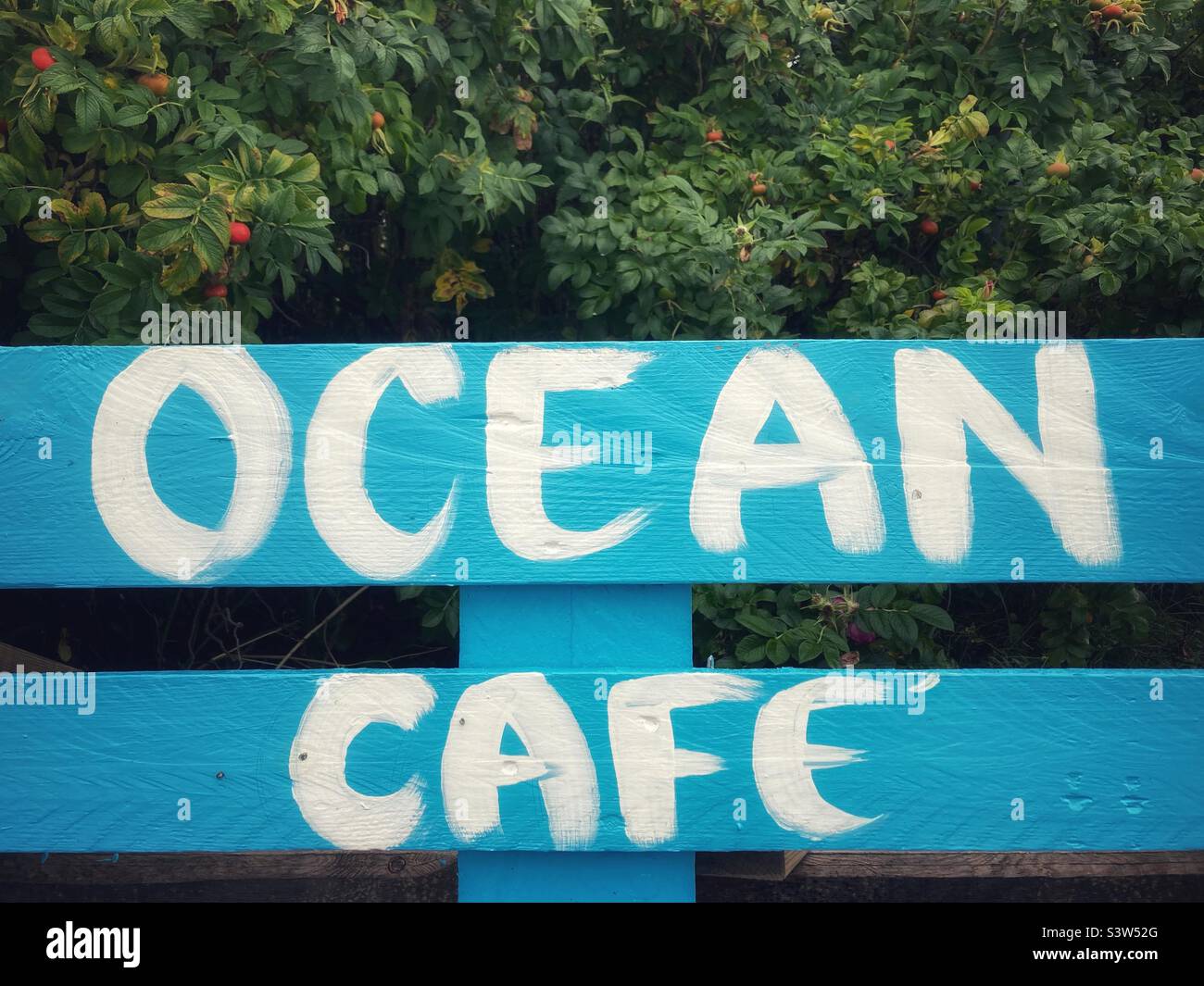 Un cartel que dice Ocean Café con letras blancas en el suelo azul Foto de stock