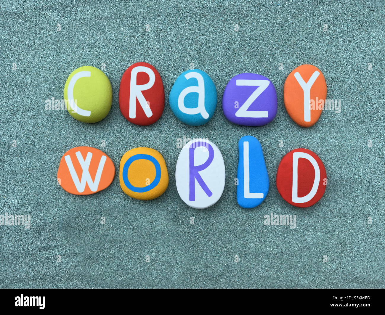 Mundo loco, texto creativo compuesto con letras de piedra multicolor sobre arena verde Foto de stock