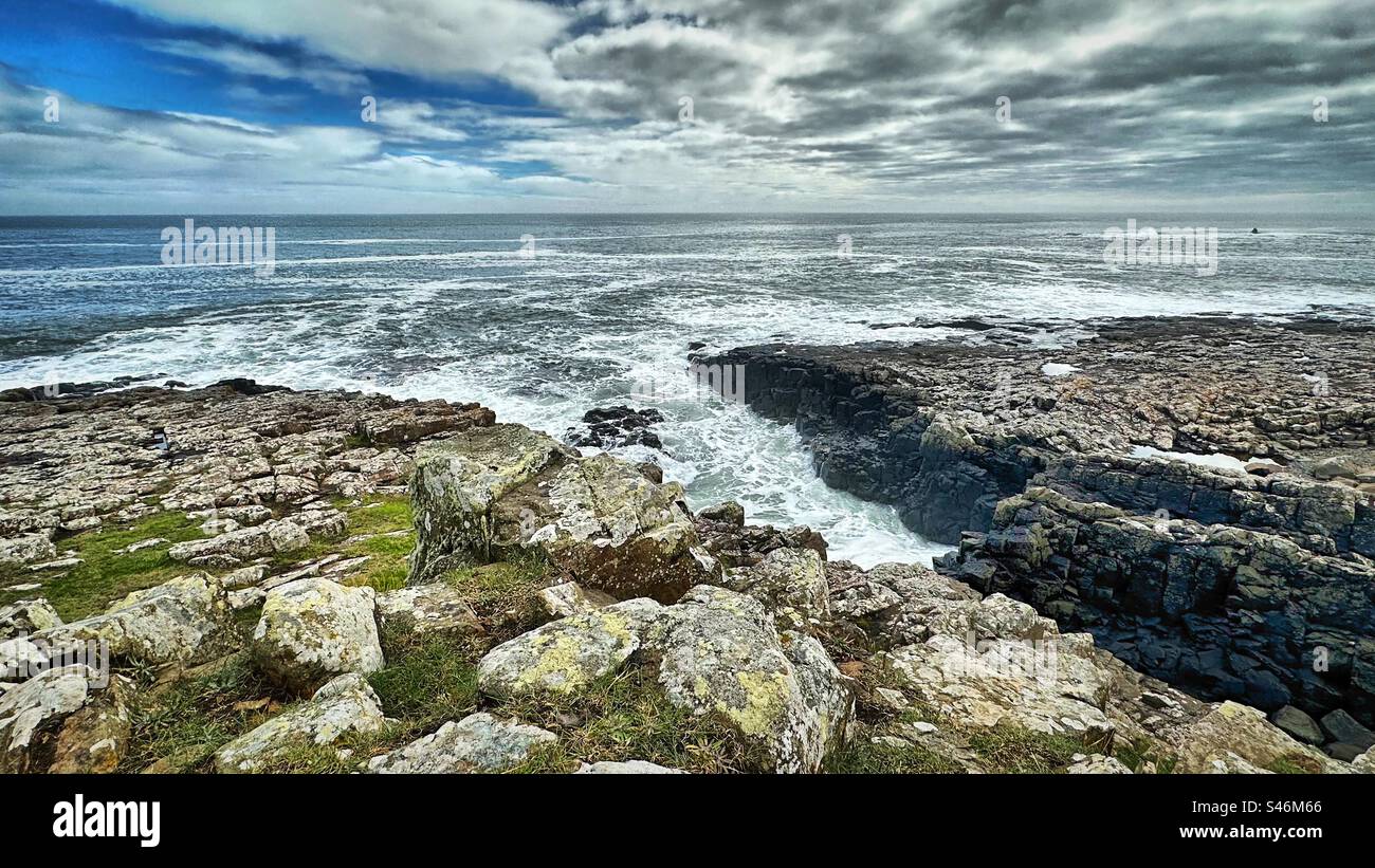 La vista desde la costa en Craster, Northumberland como las olas chocan contra las rocas en un día de clima cambiante en el mar. Foto de stock