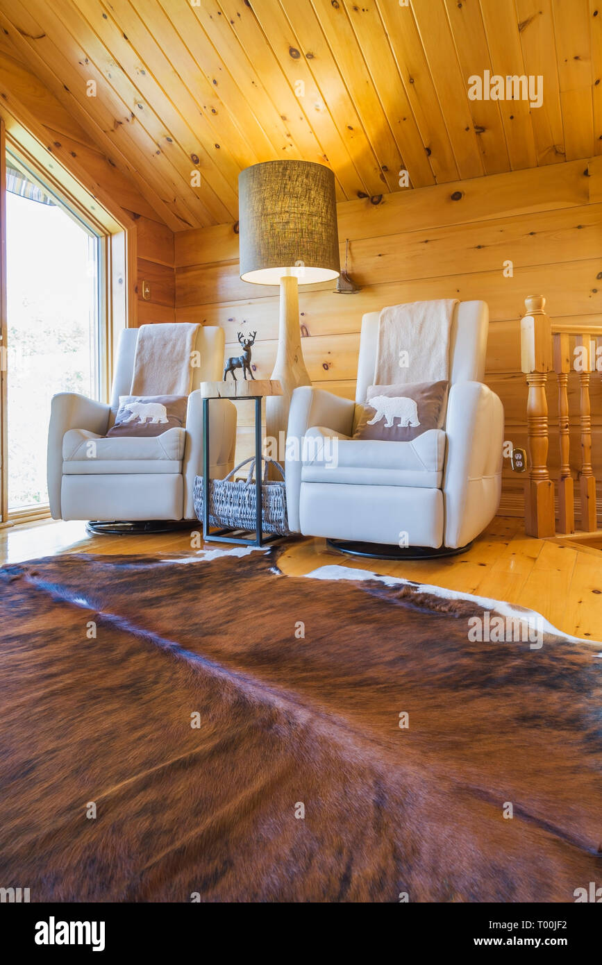 Sillones reclinables de cuero color crema con base de madera lámpara de  piso alto y alfombras de piel de vaca en el piso de arriba dentro de un  pedazo sur oriental pieza