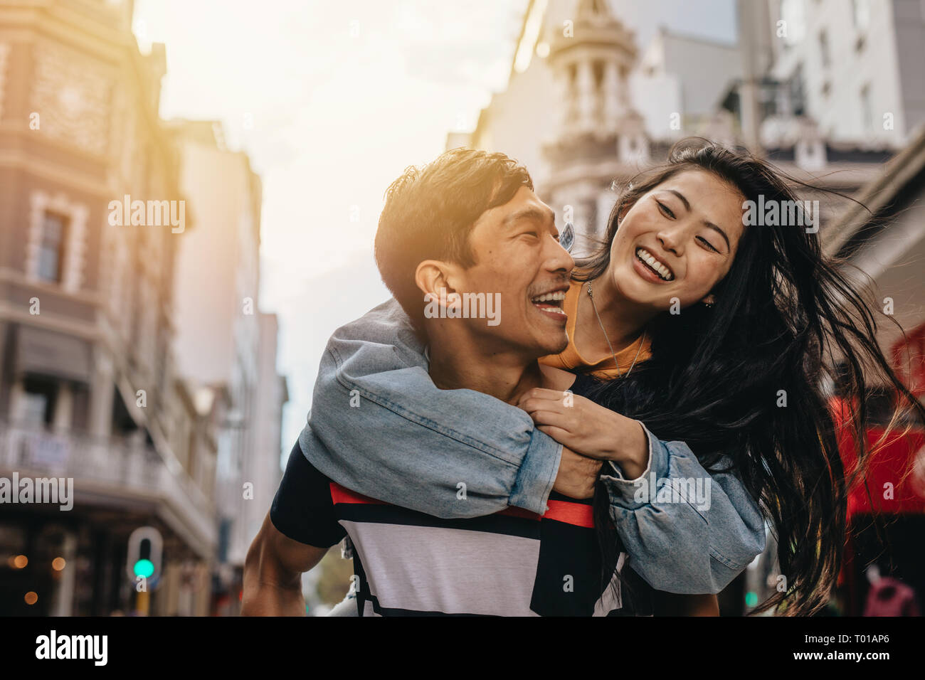 Sonriente joven dando piggyback paseo a su novia afuera en las calles de la ciudad. Pareja amorosa a divertirse al aire libre en la ciudad. Foto de stock