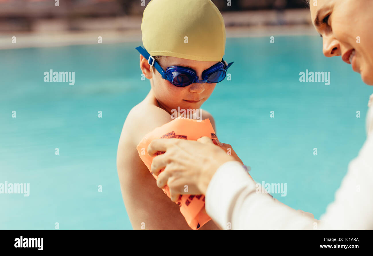 Mujer poniendo mangas flotan sobre el chico de la mano. Chico listo para  lecciones de natación en la piscina. Mujer ayudando hijo puesto en  flotadores por el brazo junto a la piscina