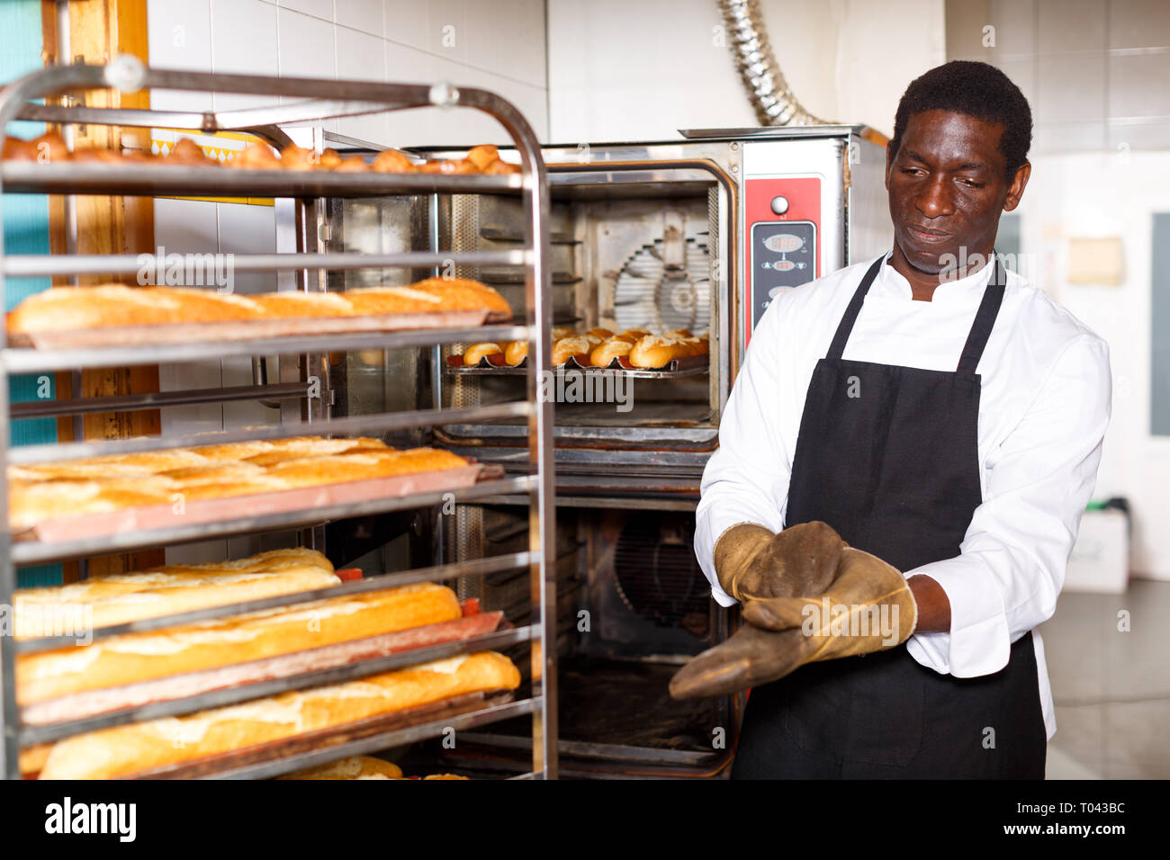 Experimentado baker Afroamericano poner guantes resistentes al calor,  listos para tomar pan cocido al horno profesional de panadería Fotografía  de stock - Alamy