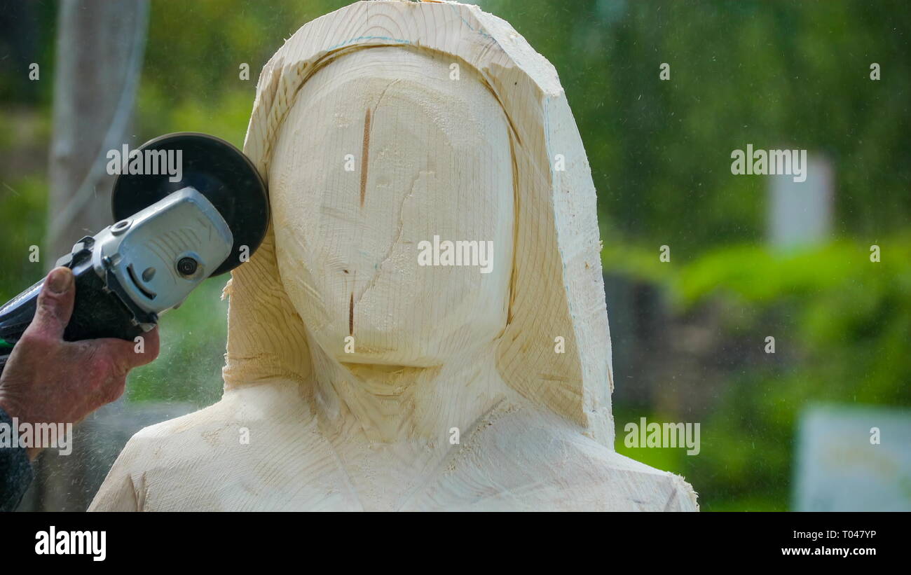 Un trabajador con un cincel eléctrico tallar las caras de una grande de  madera convirtiéndola en una imagen de una señora estatua Fotografía de  stock - Alamy